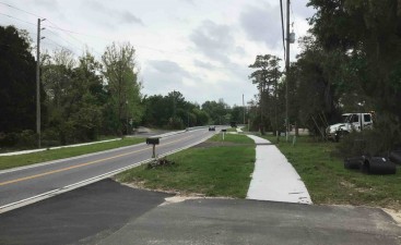 Looking south along Turkey Oak Drive at new sidewalk and driveways just north of Balloon Lane, with new guardrail in the background (3/31/2022 photo)