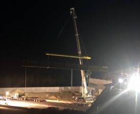 A bridge beam is lifted and ready to be swung into place (1/18/2022 photo)