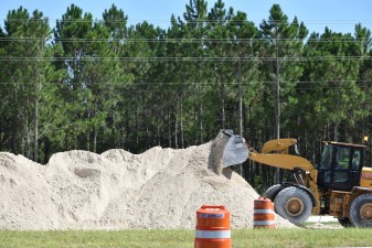 Lime rock for roadway base is stockpiled beside westbound Overpass Road (8/15/2022 photo)