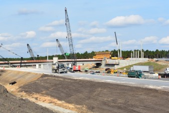 A truck hauls material on the new southbound entrance ramp with bridge construction in the background (12/9/2021 photo)