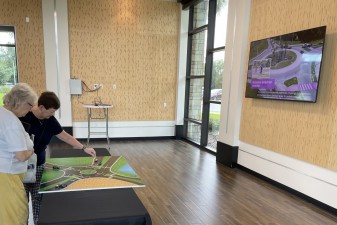 Open house visitors learn about roundabouts on a table top display and by the video playing on the wall monitor (9/10/2024 photo)