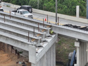 Workers carefully guide a concrete bridge beam into place over the railroad tracks (5-12-2026 photo)