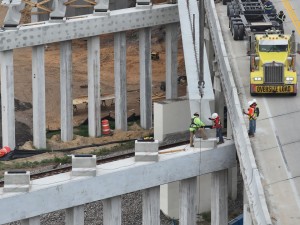 Workers carefully guide a concrete bridge beam into place over the railroad tracks (5-12-2026 photo)